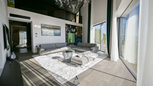 Ein modernes Wohnzimmer mit großem Fenster, einem grauen Sofa, einem Couchtisch und einem besonderen Kronleuchter.