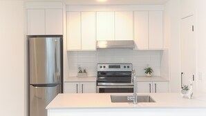 A modern kitchen with white cabinetry, stainless steel appliances, and a white countertop. - Bright & Cozy Kitsilano Suite | Walk to Beach (Vancouver)