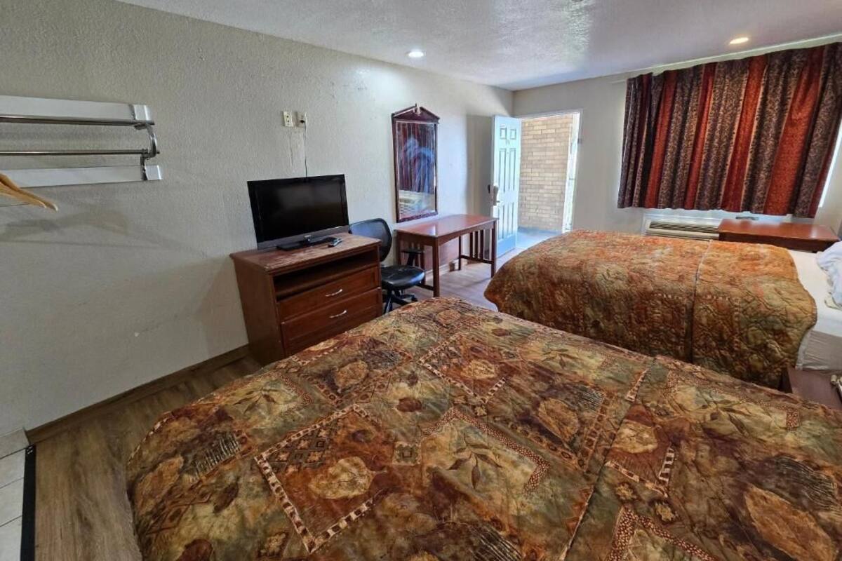 A hotel room with two beds, a desk with a chair, a television, and a window with curtains.