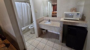 Een badkamer met douche, toilet, wastafel en een magnetron op het aanrecht.