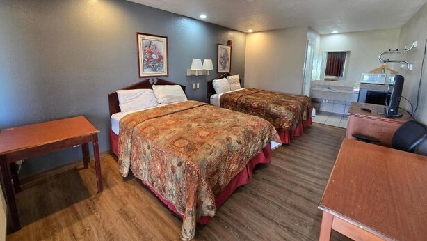 Een hotelkamer met twee bedden, een bureau, een stoel, een televisie en een badkamer die door een geopende deur zichtbaar is.