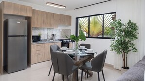 A modern kitchen with wooden cabinets, a stainless steel refrigerator, a dining table set for four, and a large window with a view of palm trees. - Plaza Colonial Residence By YellowKey (Santo Domingo)