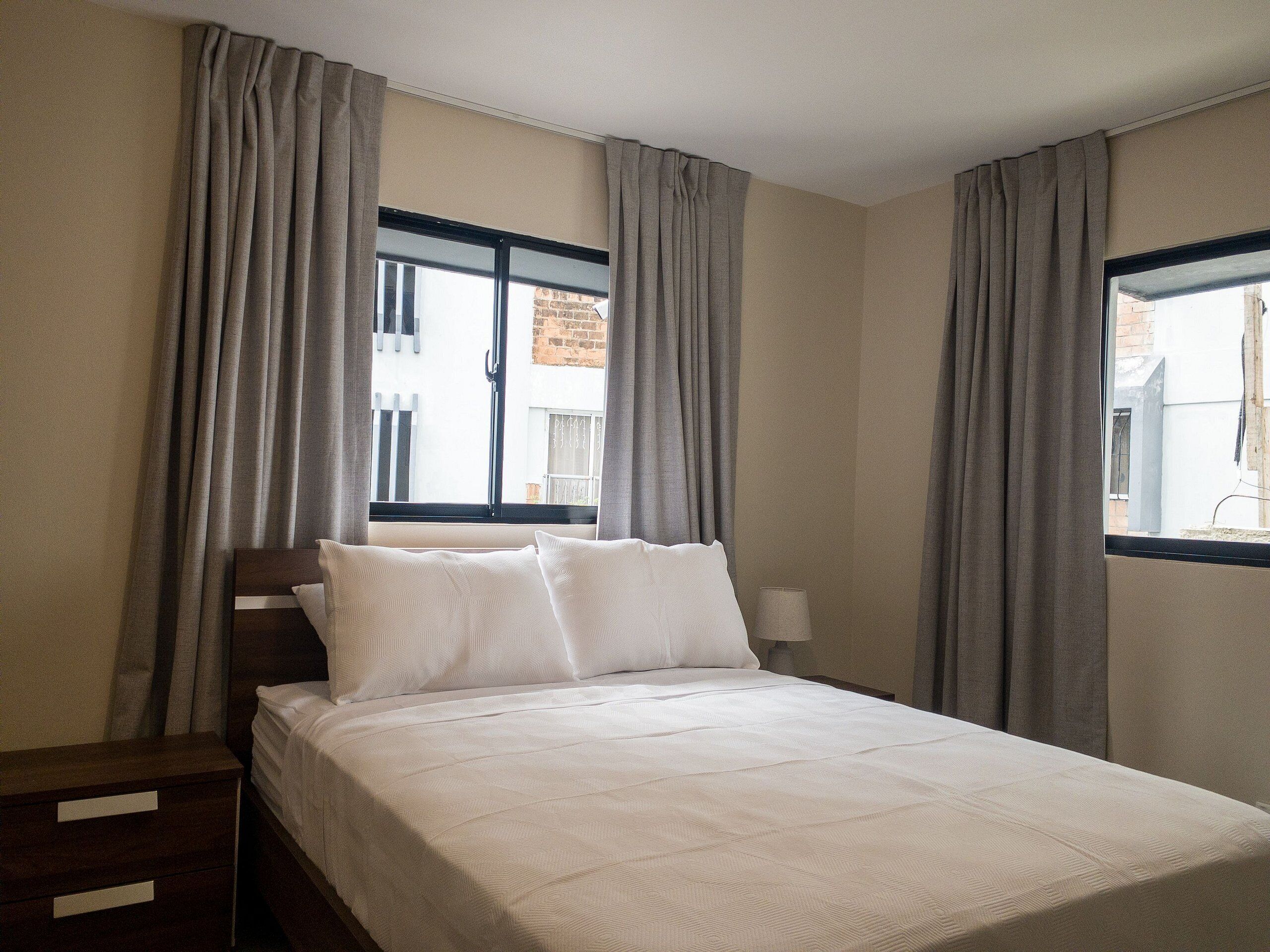 A bedroom with a bed, curtains, a nightstand, and a window.