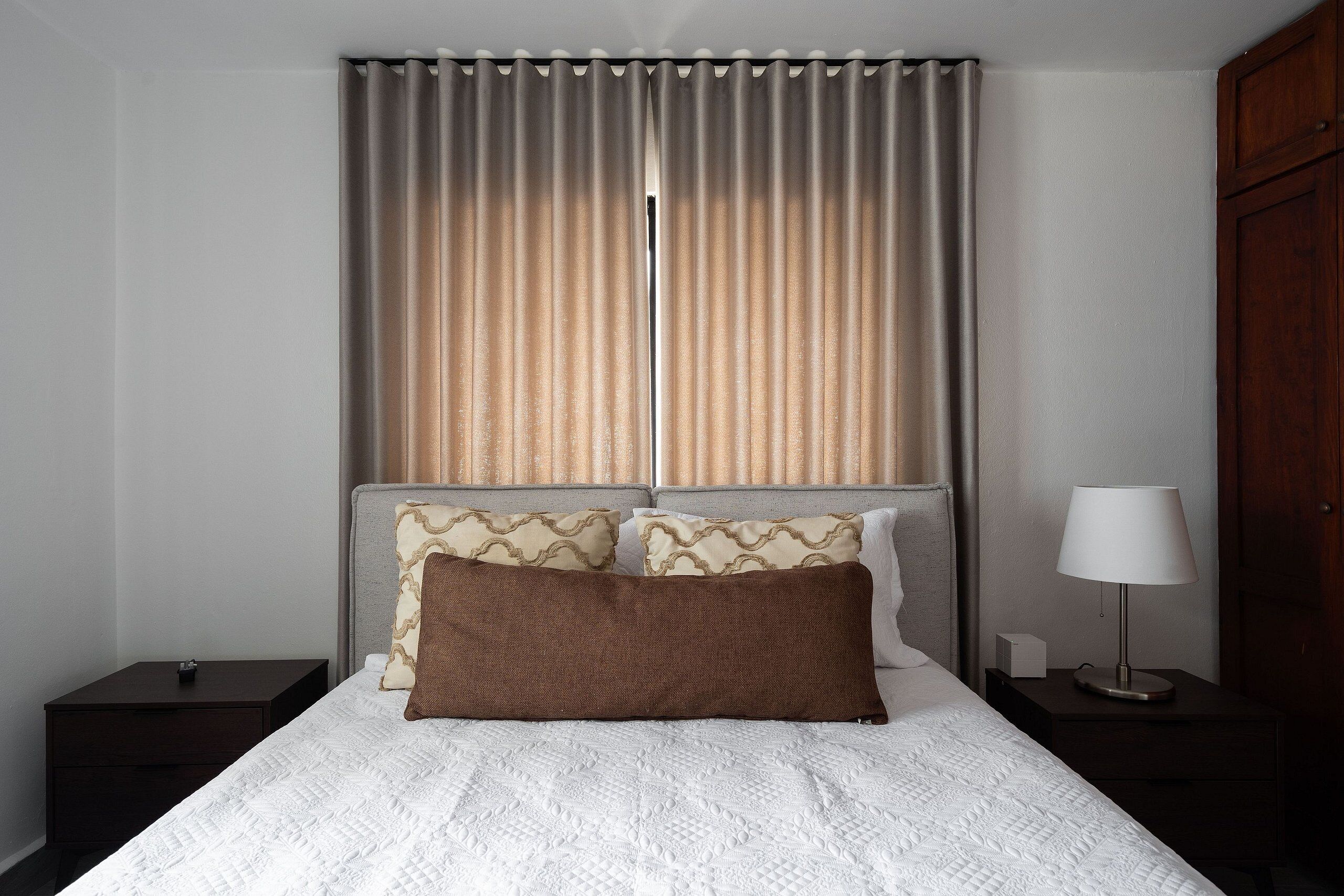 Una cama bien tendida con colcha blanca, dos almohadas, una lámpara de noche y una mesita de noche.
