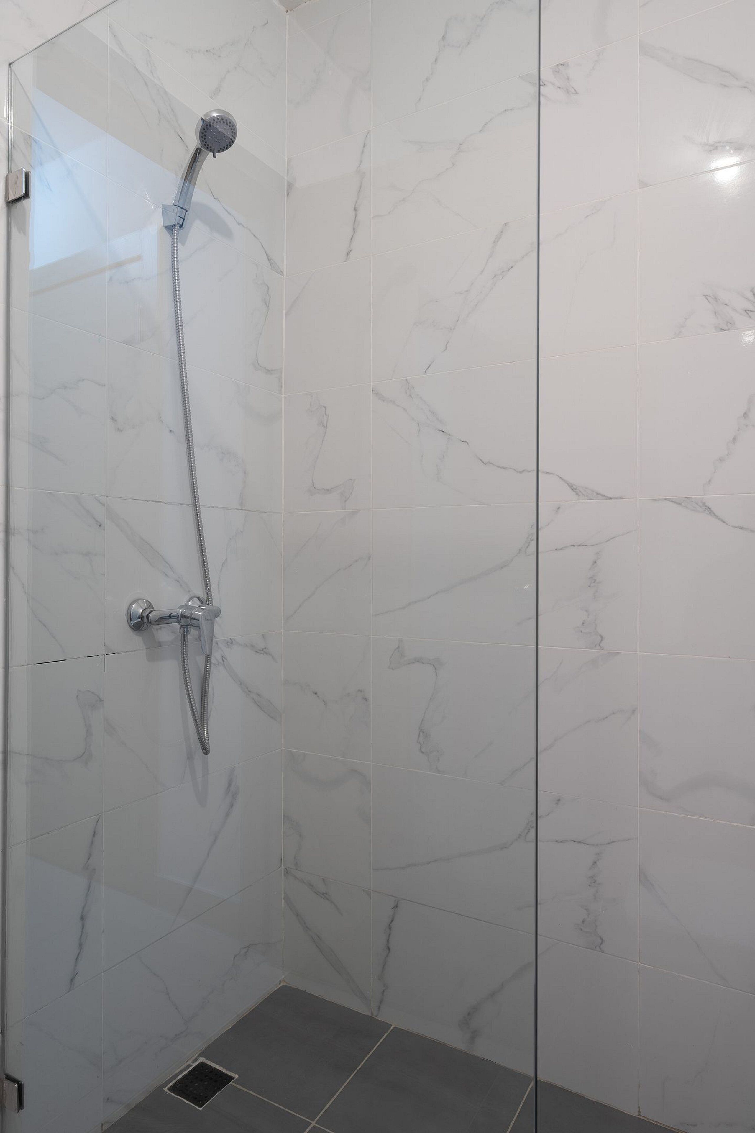 A glass-enclosed shower with a handheld showerhead and a wall-mounted faucet.