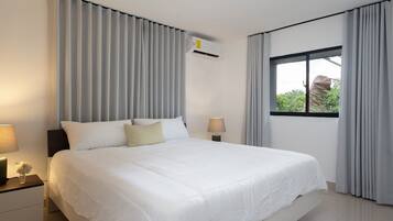 A modern hotel room with a large bed, a nightstand with a lamp, a window with curtains, and an air conditioning unit.