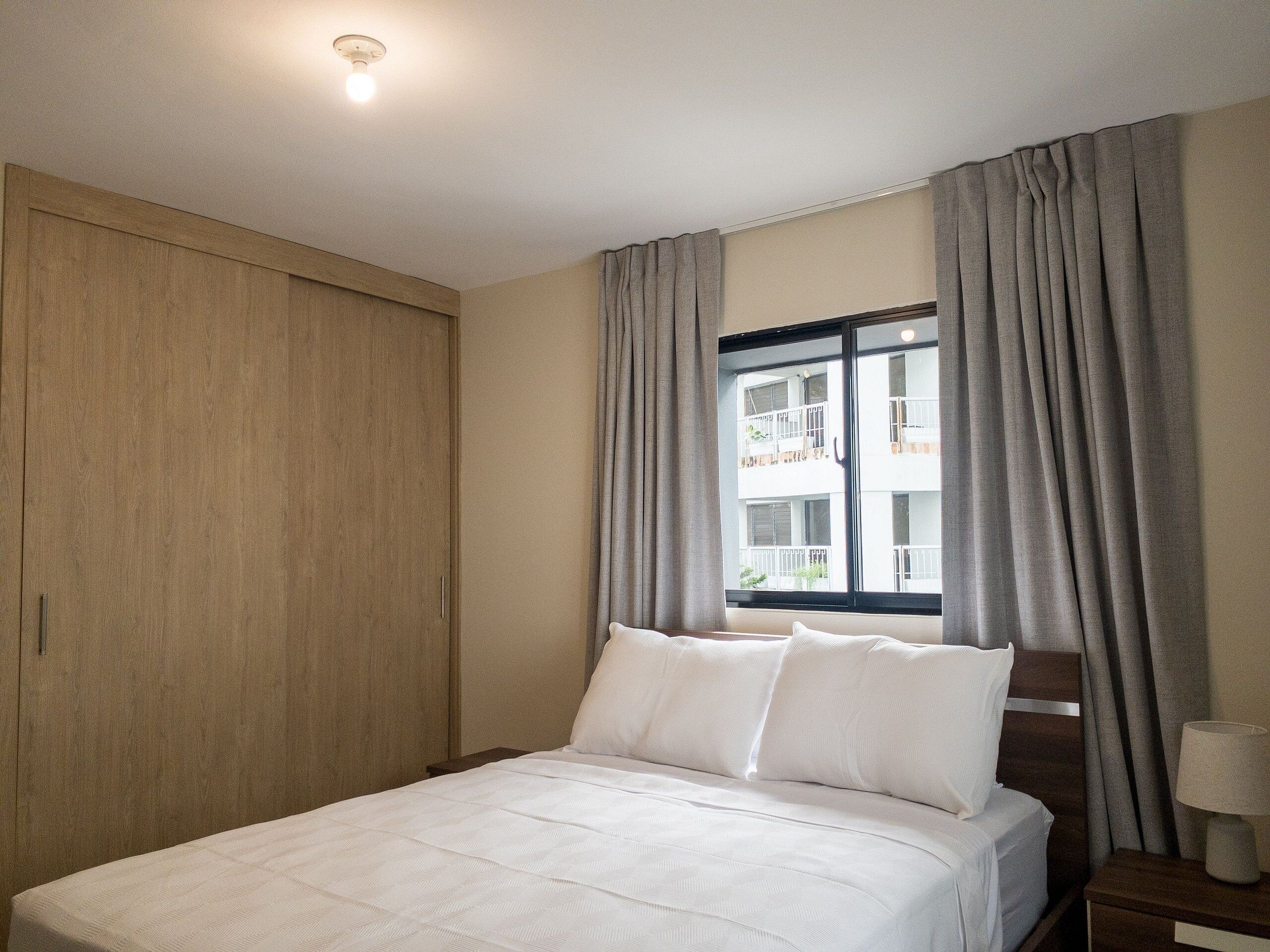 A hotel room with a bed, a nightstand, a lamp, and a window with curtains.