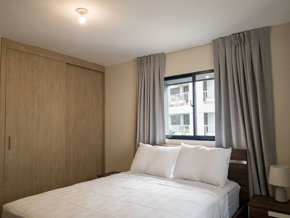A hotel room with a bed, a nightstand, a lamp, and a window with curtains.