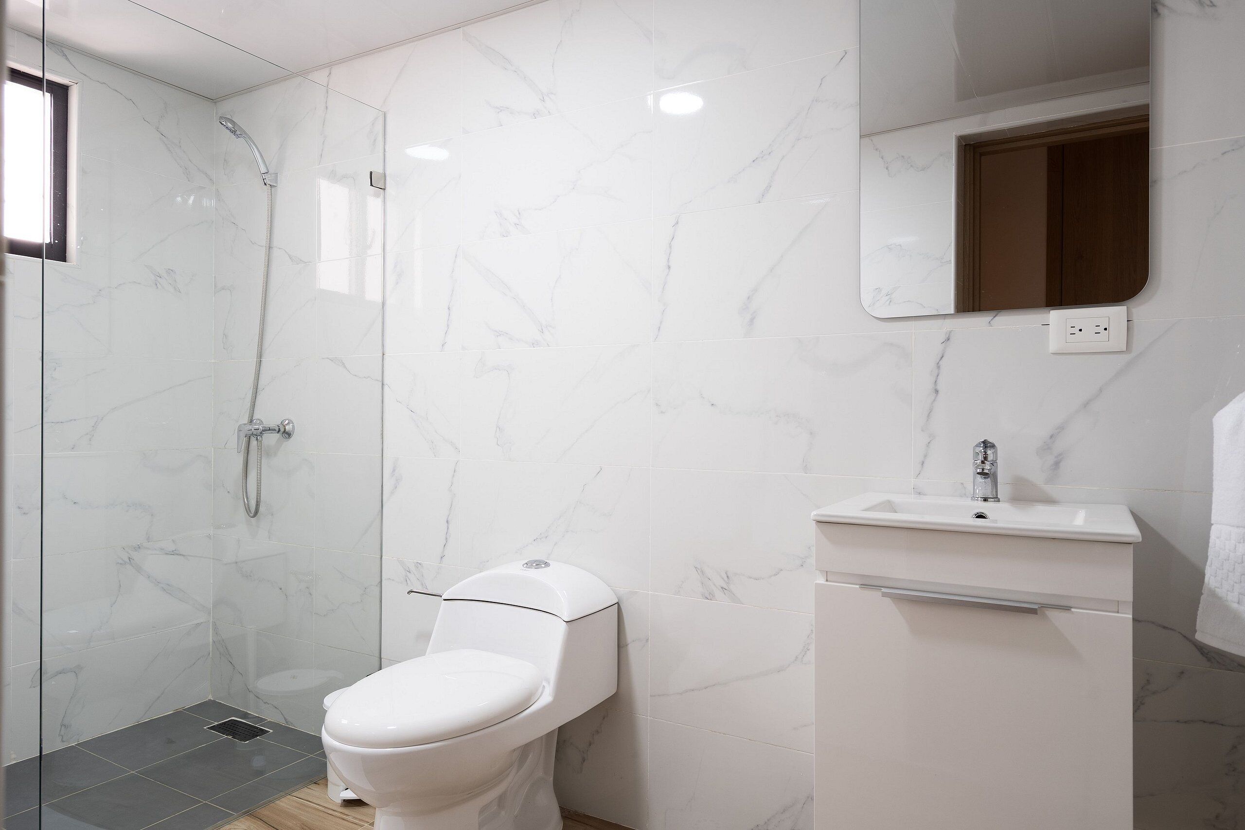 Un baño moderno con ducha envuelta en vidrio, inodoro y lavamanos con espejo superior.