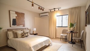 A bedroom with a bed, bedside table, lamp, chair, and a window with curtains. - Plaza Colonial Residence By YellowKey (Santo Domingo)