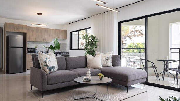 A modern living room with a grey sectional sofa, a coffee table, and a view of the kitchen and balcony. - Plaza Colonial Residence By YellowKey (Santo Domingo)