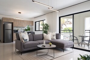 A modern living room with a grey sectional sofa, a coffee table, and a view of the kitchen and balcony.