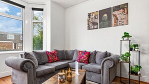Una sala moderna con un sofá seccional gris, una mesa de centro de madera con velas y un estante alto para plantas.