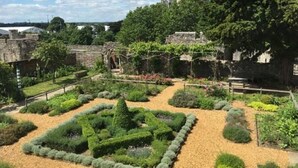 Un jardín con arreglos geométricos de plantas y un muro de piedra.