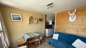Ein gemütliches Zimmer mit einem blauen Sofa, einem Holzesstisch mit Stühlen, einer Küchenzeile und einem aufgehängten Hirschkopf an der Wand.