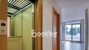 Een hotelgang met een lift, een deur naar een receptie en uitzicht buiten.