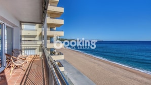 Een vakantiehuis aan het strand met een balkon dat uitkijkt over de zee, met rieten stoelen en een betegelde vloer.