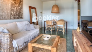 Een moderne woonkamer met een bank, een salontafel met glazen blad, rieten stoelen en een eettafel.