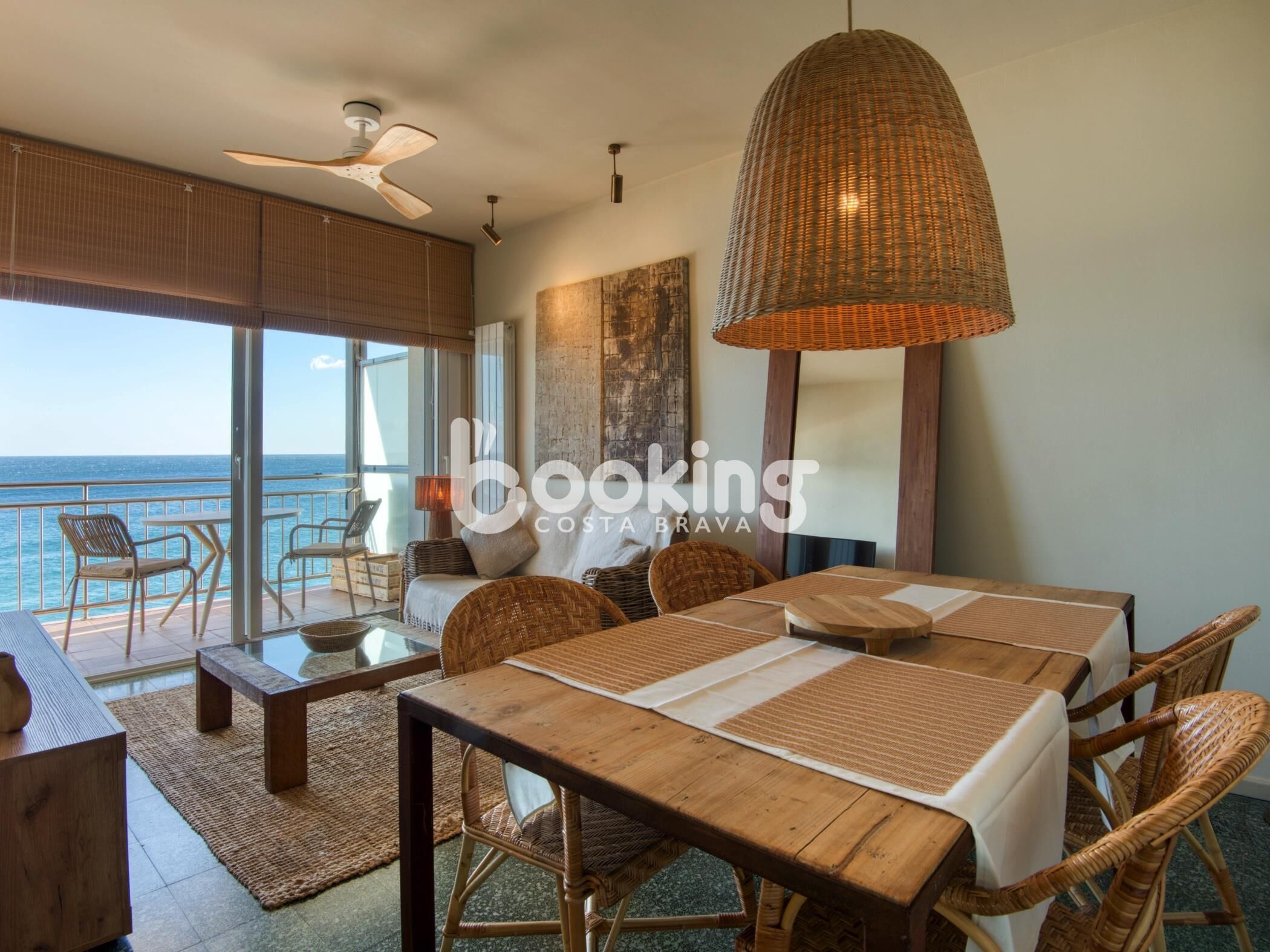 Zona pranzo con vista sull'oceano, caratterizzata da mobili in vimini, un lampadario ampio e una ventola a soffitto.