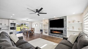A modern living room with a grey sofa, a fireplace, a flat-screen TV, and a dining area with a table and chairs. - Golf & Beach Retreat Firepit BBQ Near Boca Grande (Rotonda West)