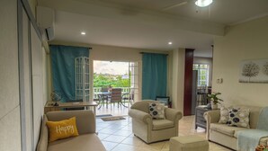 A living room with a sofa, armchairs, and a coffee table. There is a dining area with a table and chairs in the background. - Sundrift Apartments (Gros Islet)