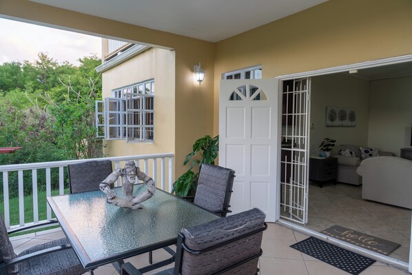 An outdoor patio with a glass table, wicker chairs, and a decorative sculpture. - Sundrift Apartments (Gros Islet)