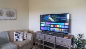 A living room with a flat-screen TV mounted on a wooden cabinet, a beige sofa with patterned cushions, and a painting on the wall. - Sundrift Apartments (Gros Islet)