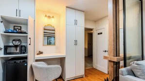 Un espace de vie compact comprenant un coin cuisine, un bureau avec un miroir, un fauteuil gris et une porte coulissante à cadre en bois.