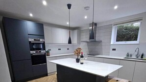 A modern kitchen with a central island, built-in appliances, and a window providing natural light. - The Minimalist's Retreat Oxford (Oxford)