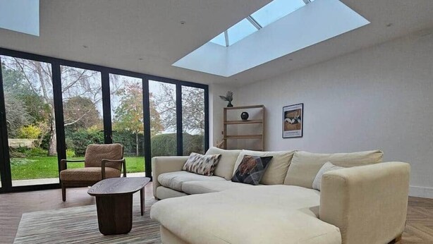 A modern living room with a large sectional sofa, a small round coffee table, and a view of a garden through large windows. - The Minimalist's Retreat Oxford (Oxford)