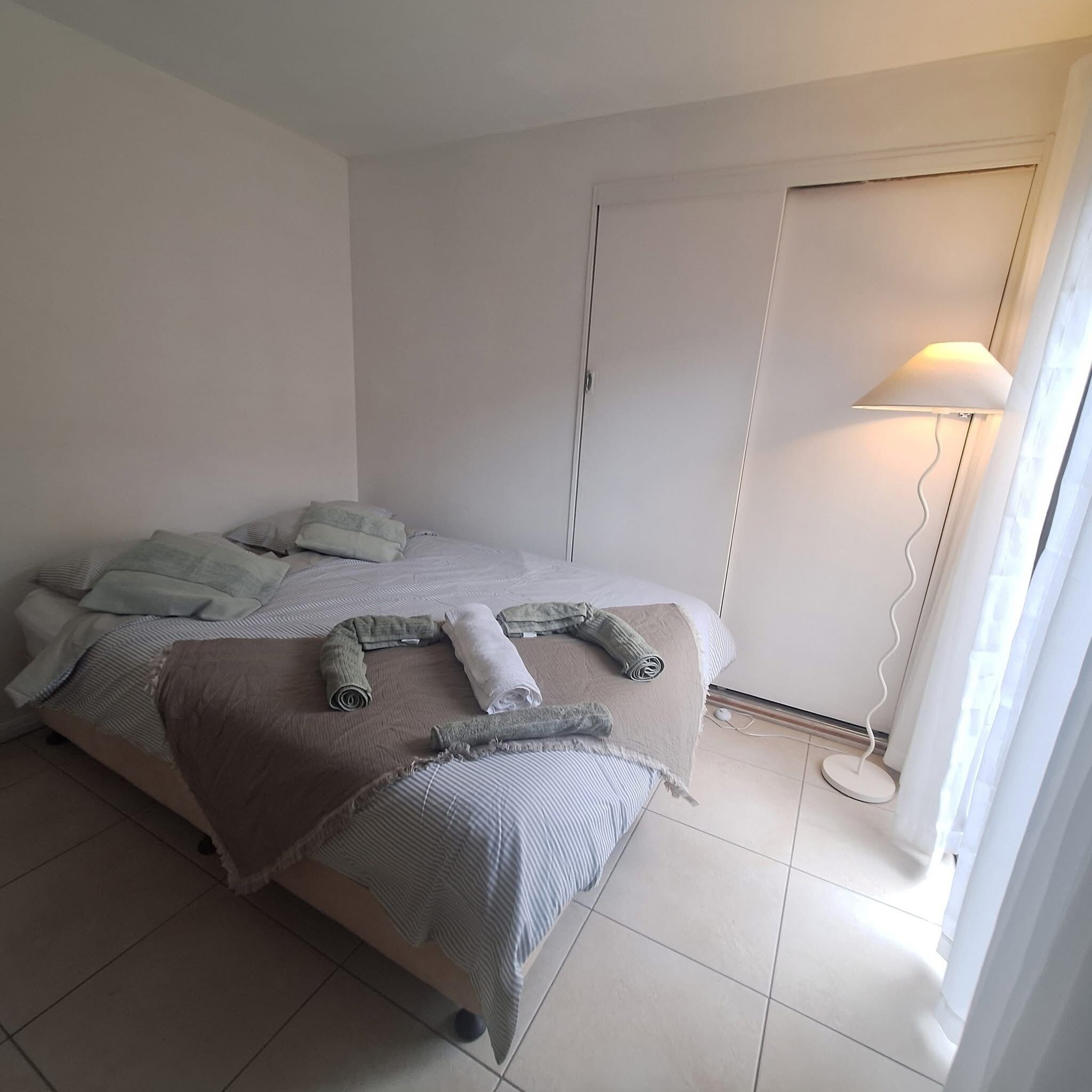 A bedroom with a bed, pillows, a bedside lamp, and a window with curtains.