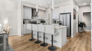 Una cocina moderna con armarios blancos, una isla central con taburetes de bar, electrodomésticos de acero inoxidable y piso de madera.