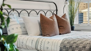 Una cama con estructura metálica, ropa de cama estampada y dos almohadas.