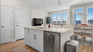 Una cocina moderna con armarios blancos, lavavajillas integrado y un comedor con sofá gris y sillas de madera.