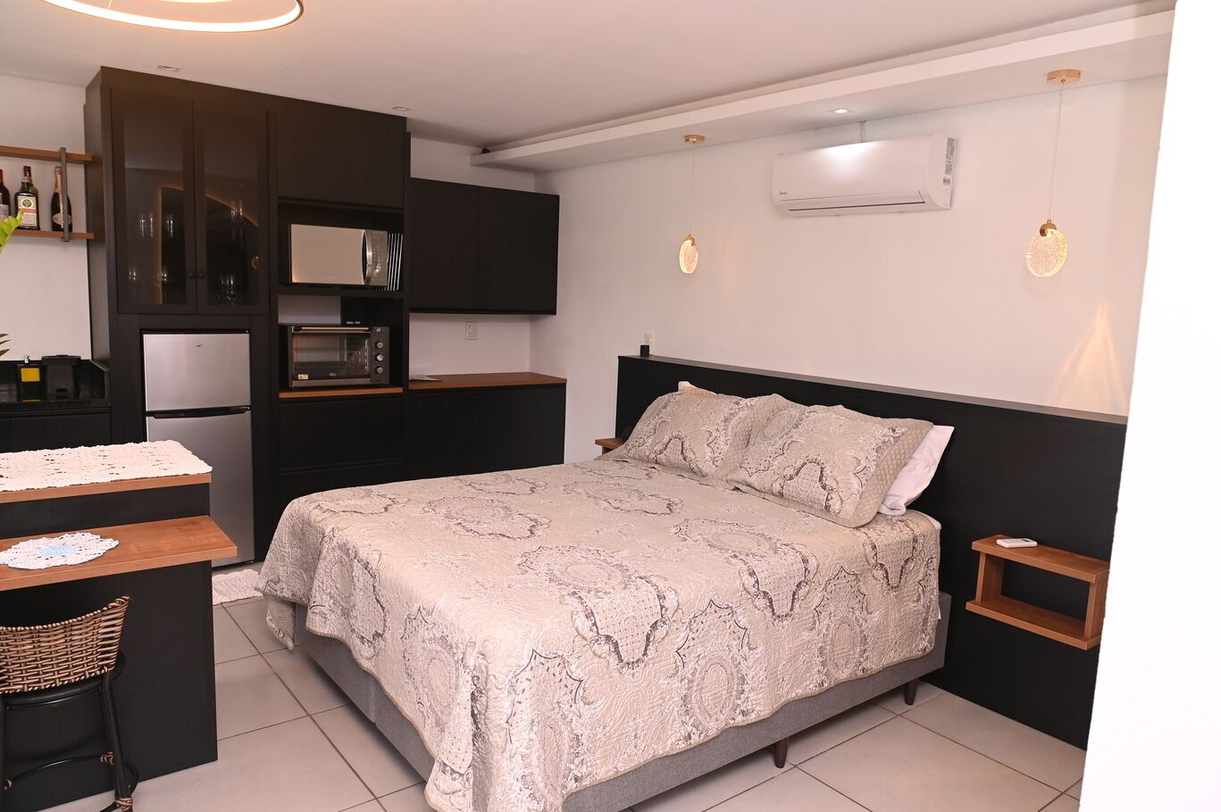 Een compacte hotelkamer met een bed, een klein bureau, een kitchenette en een nachtkastje.
