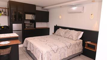 Een compacte hotelkamer met een bed, een klein bureau, een kitchenette en een nachtkastje.