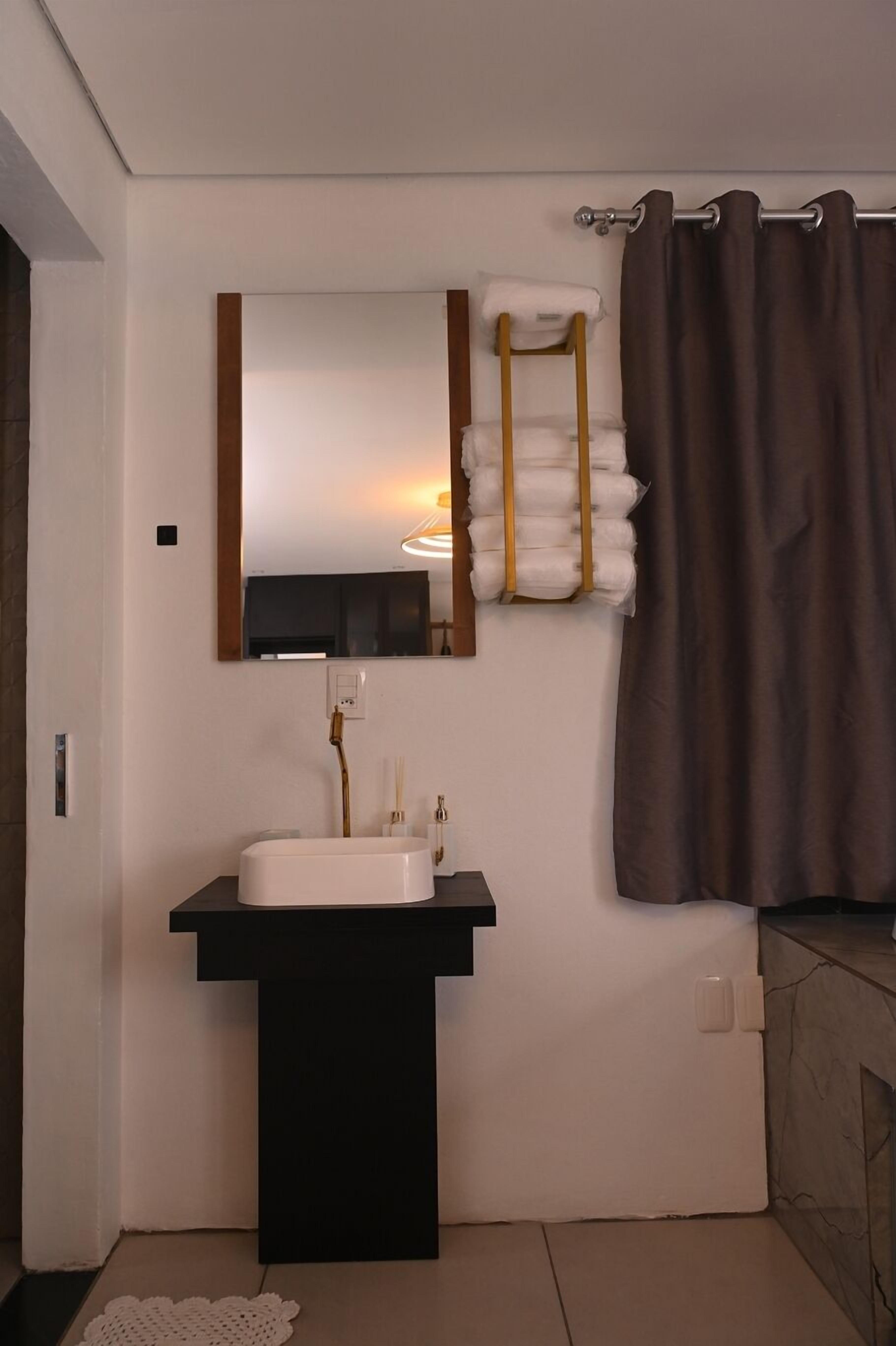 A bathroom with a black sink, a mirror, a towel rack with towels, and a shower curtain.