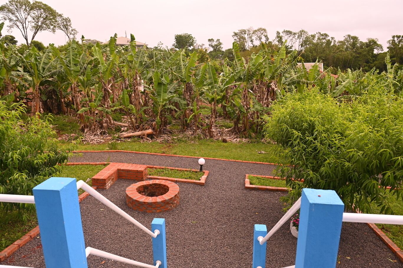 A garden area with a brick fire pit, surrounded by gravel and bordered by blue and white railings.