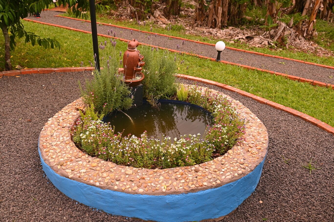 Ein kreisförmiger Garten mit einem Teich, umgeben von einem Kiesstreifen und einem blauen Rand.