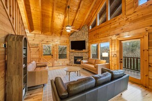 A log cabin interior with a stone fireplace, leather sofas, and a flat-screen TV. - 5 Min to PF Pkwy • New 7' Cedar Hot Tub • Mtn View • Game Room • Pet Friendly (Pigeon Forge)