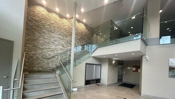 A modern lobby with a stone wall, a glass staircase, and a reception desk. - 5 min walk to university with stunning mountain views (Kelowna)