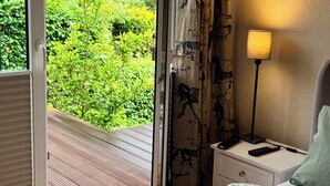Un dormitorio con cama, mesita de noche, lámpara y vistas a la vegetación a través de una puerta corrediza de vidrio.