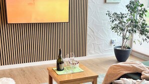 Una sala de estar moderna con un revestimiento de listones de madera, un televisor de pantalla plana, un sofá verde, una mesa de centro con una botella y vasos, una planta en maceta y un control remoto sobre el sofá.