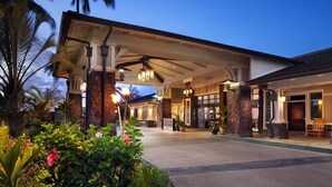 Entrada de hotel com varanda coberta, pilares de pedra e fachada bem iluminada.