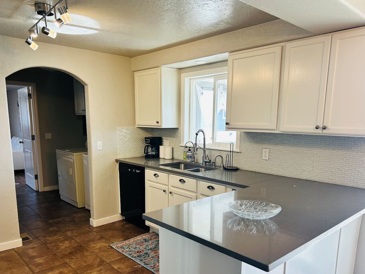 A kitchen with white cabinets, a black countertop, a window, and a dishwasher.