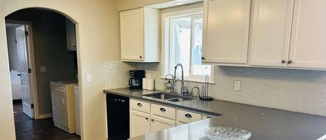 A kitchen with white cabinets, a black countertop, a window, and a dishwasher.