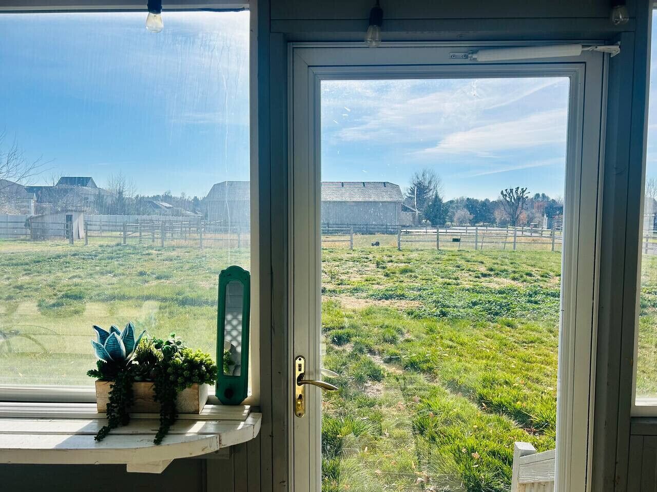 Een kamer met een groot raam met uitzicht op een grasveld en gebouwen in de verte.