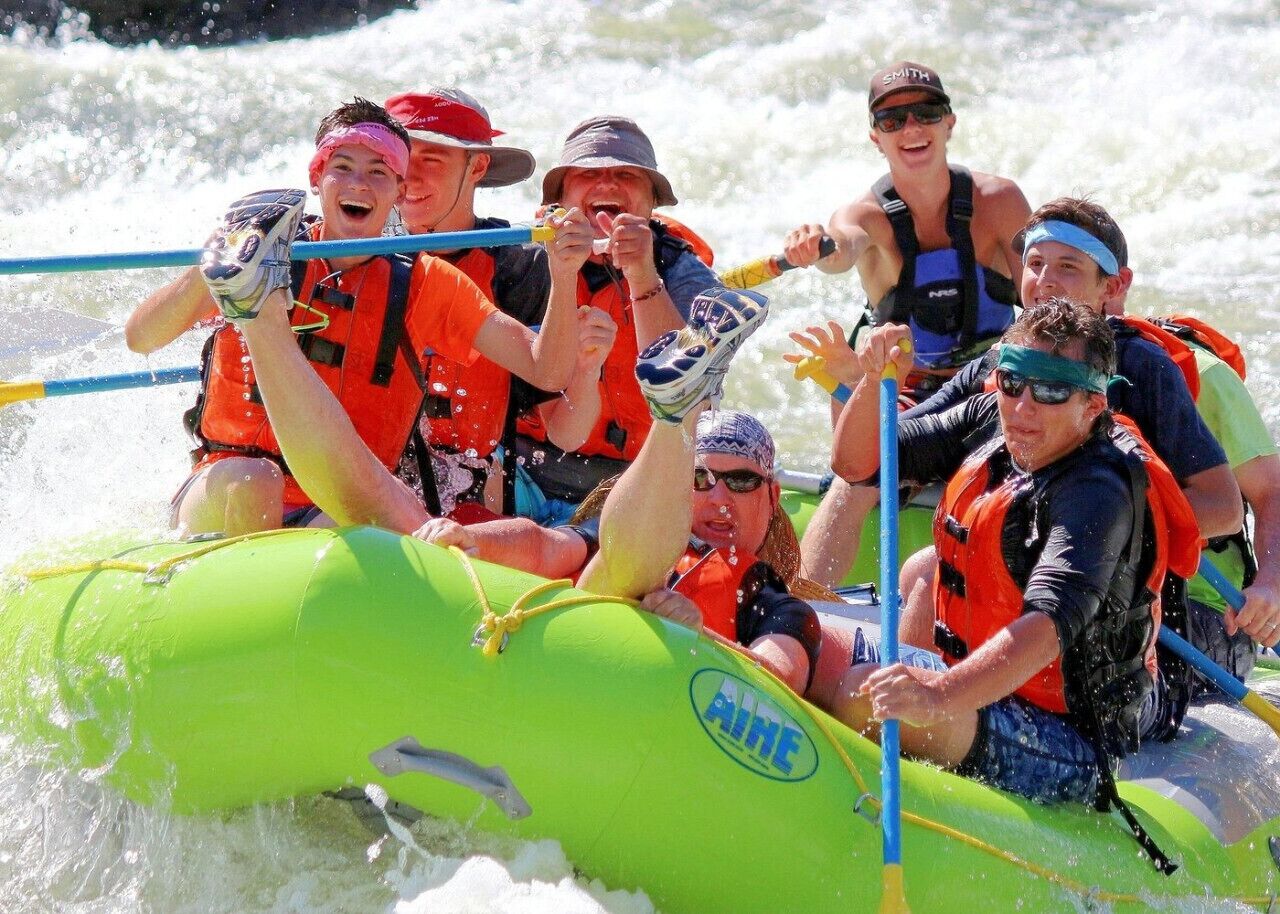 A group of people in a raft with life jackets, paddling on a river.