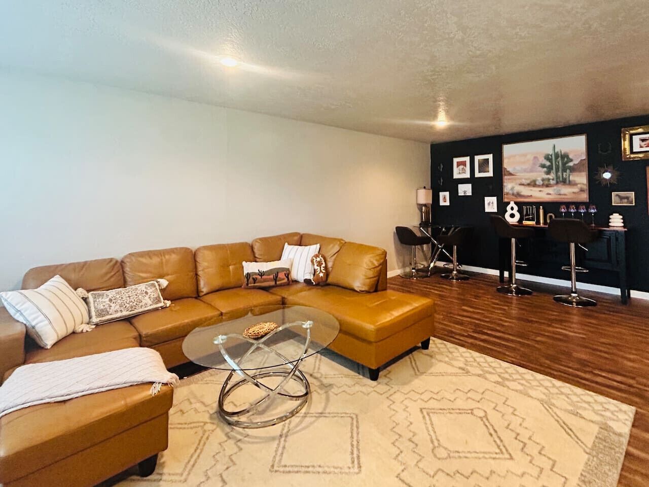 A modern living room with a brown leather sectional sofa, a glass coffee table, and a patterned rug.