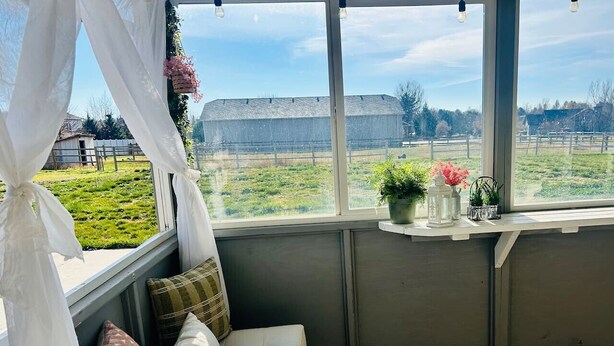 A cozy room with a cushioned bench, a view of a green field, and a window with a white curtain. - Bonanza Blast in SW Boise (Boise)